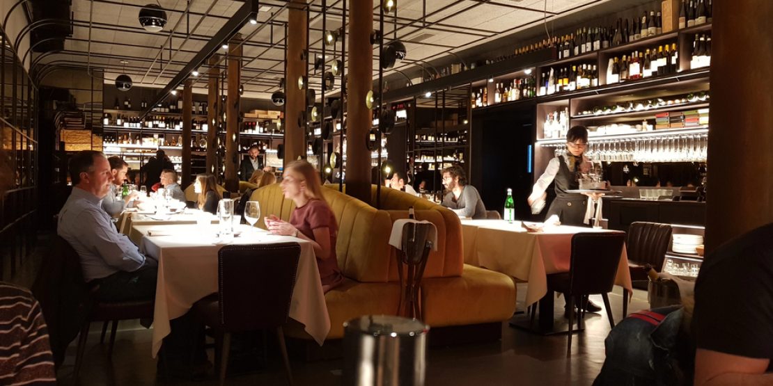 Busy dining room with patrons and staff in a noisy restaurant, highlighting acceptable noise levels in restaurants and ideas on how to reduce noise in a restaurant for better ambience.