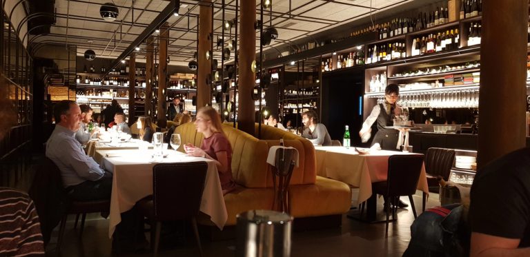 Busy dining room with patrons and staff in a noisy restaurant, highlighting acceptable noise levels in restaurants and ideas on how to reduce noise in a restaurant for better ambience.